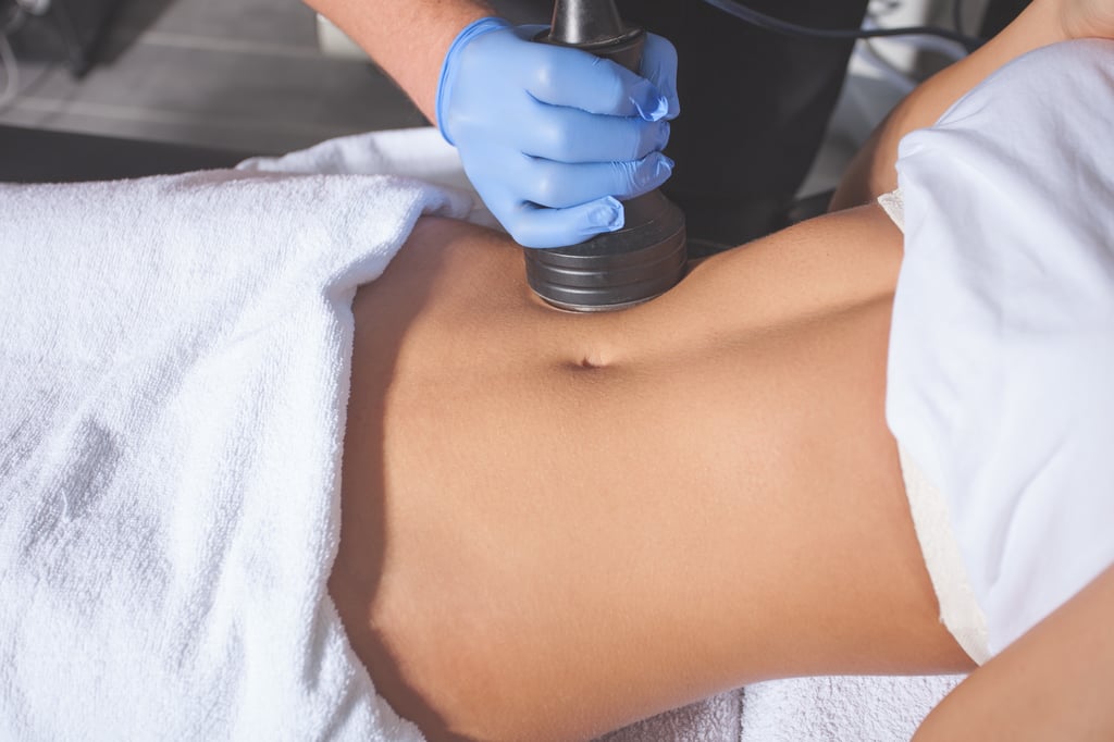 Gloved hand uses body contouring device on abdomen covered with white towels