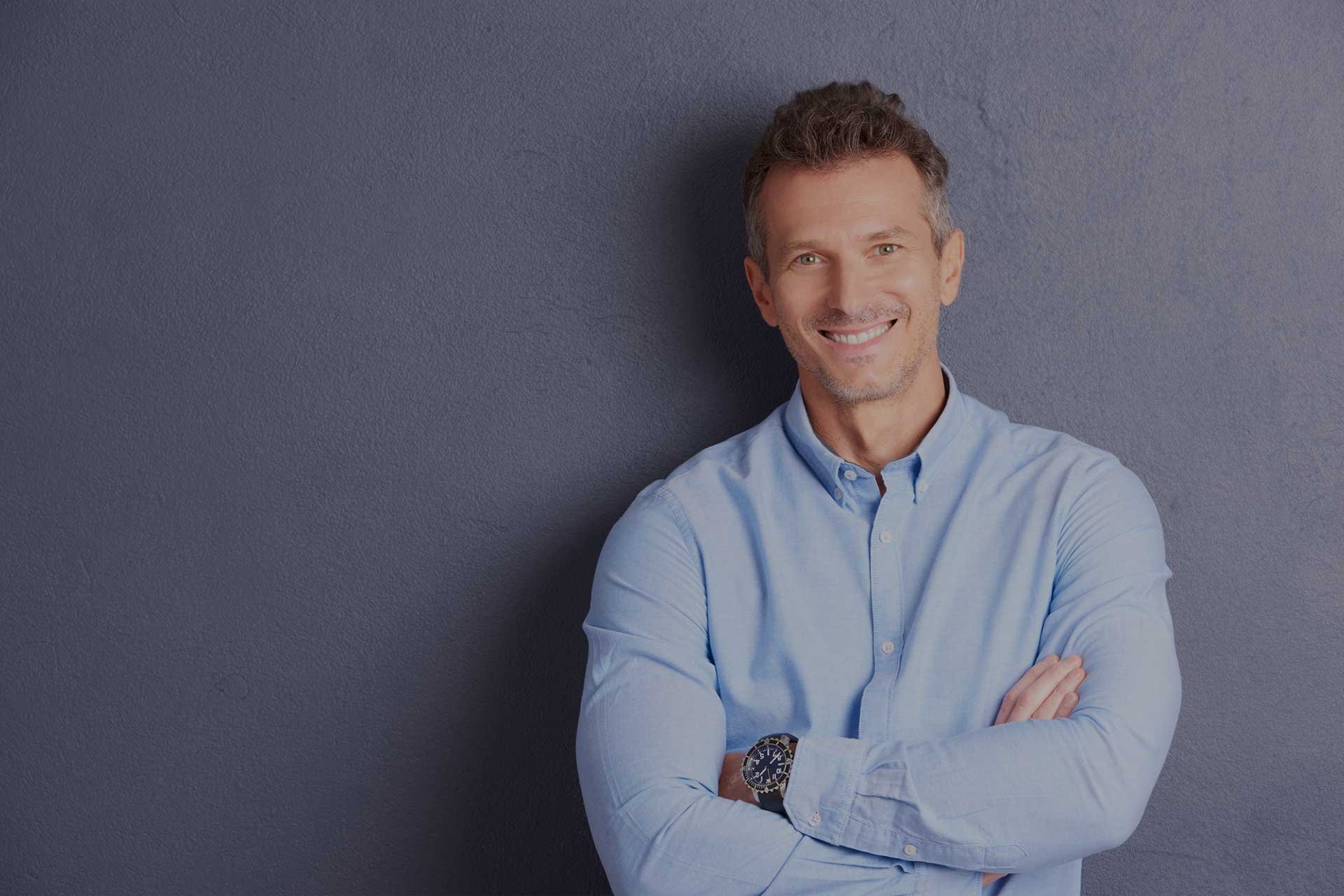 Portrait of middle aged businessman wearing shirt and looking at camera while standing at grey background.