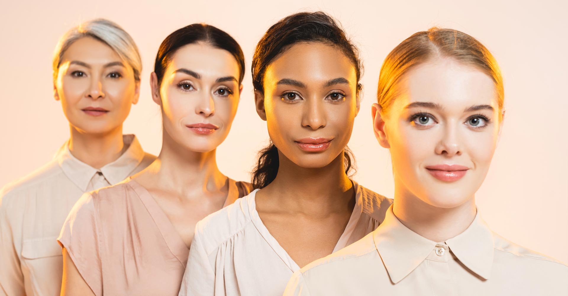 Selective focus of happy multicultural women looking at camera isolated on beige