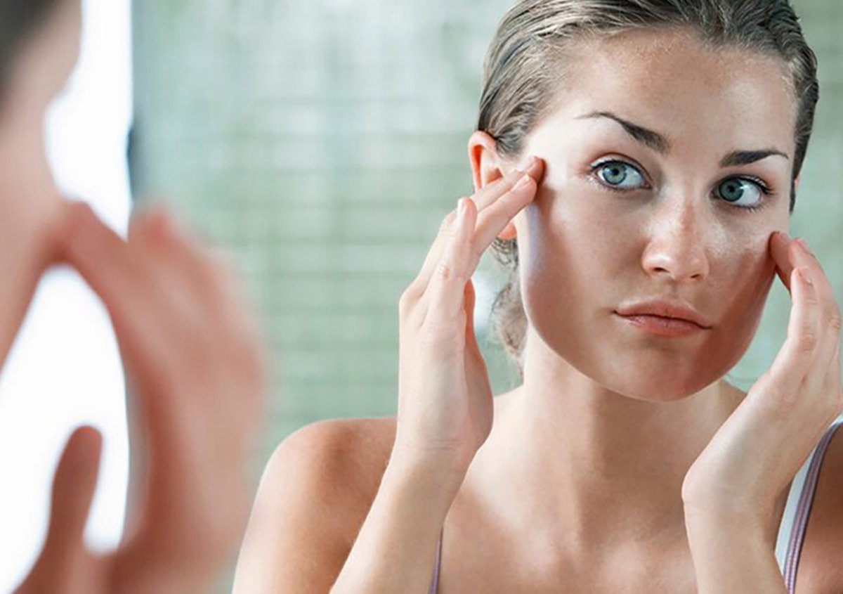 Person examining facial skin in mirror, highlighting rejuvenation and results of endoscopic brow lift and eyebrow lift surgery in Norwalk, CT