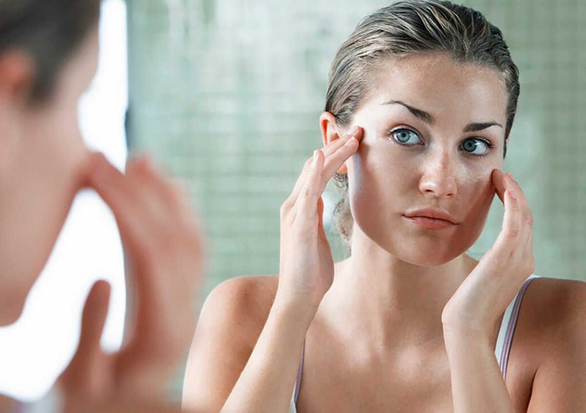 Patient examining under-eye area in mirror before cosmetic eyelid surgery for bags in Norwalk, CT