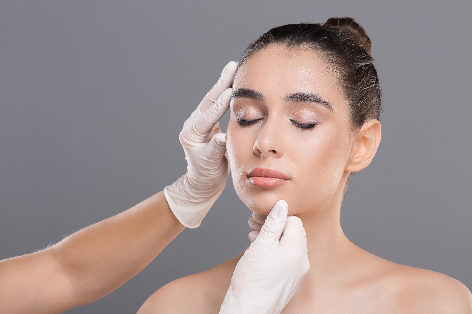 Woman receiving facial assessment from clinician wearing gloves in aesthetic setting